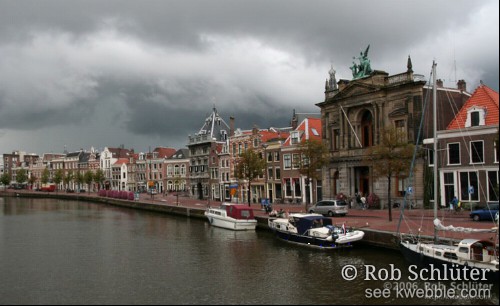 Dreigende lucht boven de oever van het Spaarne met hischorische gebouwen waaronder het Teylers museum.