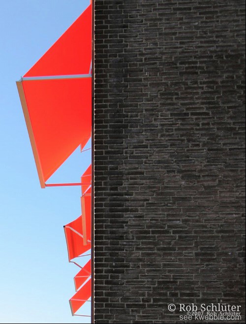 Fel oranje zonneschermen steken uit een bakstenen muur.