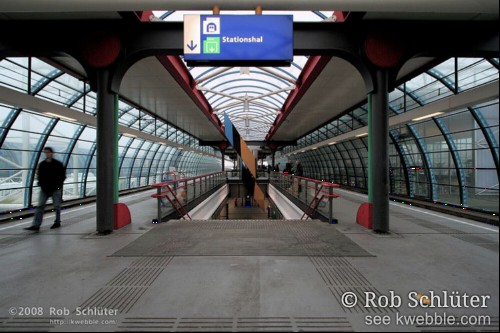 Perron met treinsporen met een doorzichtige kokervormige overkapping en het gat van de trap naar beneden.